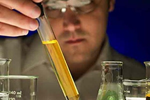 A man looks closely at a test tube filled with yellow liquid