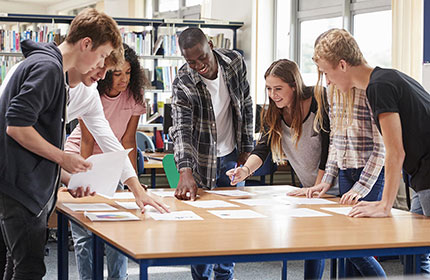 A group of college students stand around a large table covered in papers