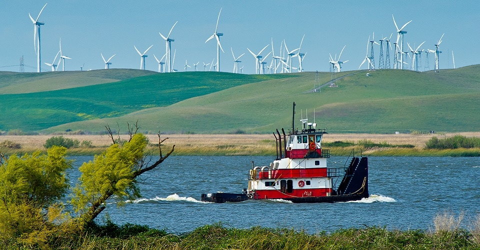 Wind power plant on river bend with boat floating in river