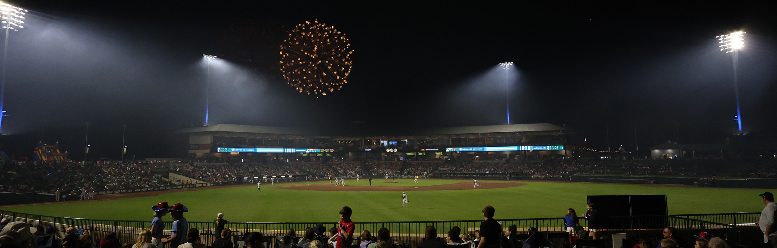 view of Dow Diamond's lights from the outfield lawn seats with fireworks in the night sky