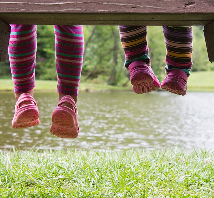 two kids legs dangling from a bench wearing Crocs