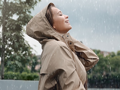 Woman with raincoat walking under rain in park