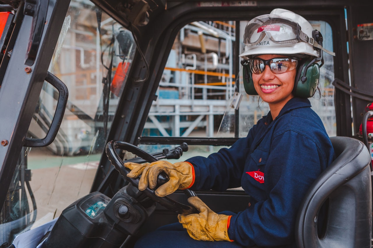 Young female employee sitting in the driver's seat of a forklift, smiling at the camera at BahÃ­a Blanca facility.