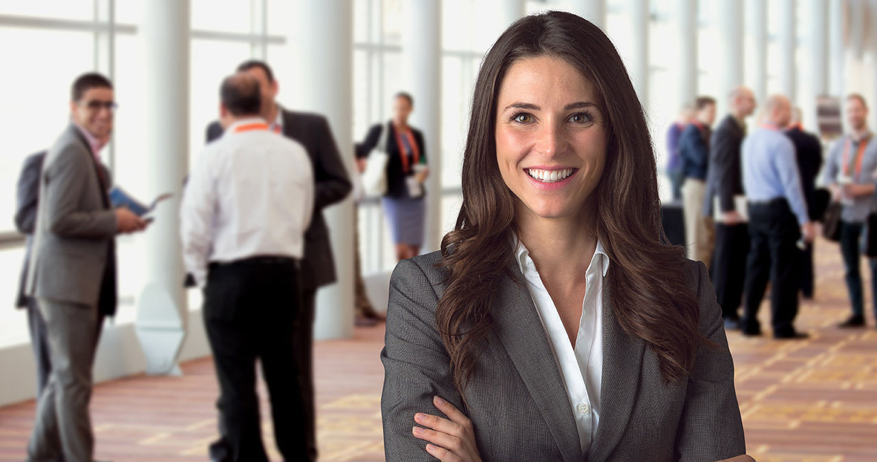 Smiling woman in foreground, with other colleagues in large room in background