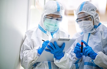 two lab workers in full protective gear examine a sample