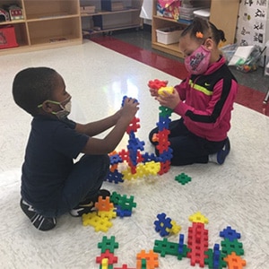 Two students in face masks playing with blocks