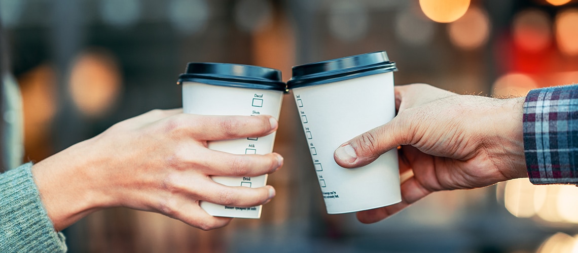 two people toasting their paper coffee cups
