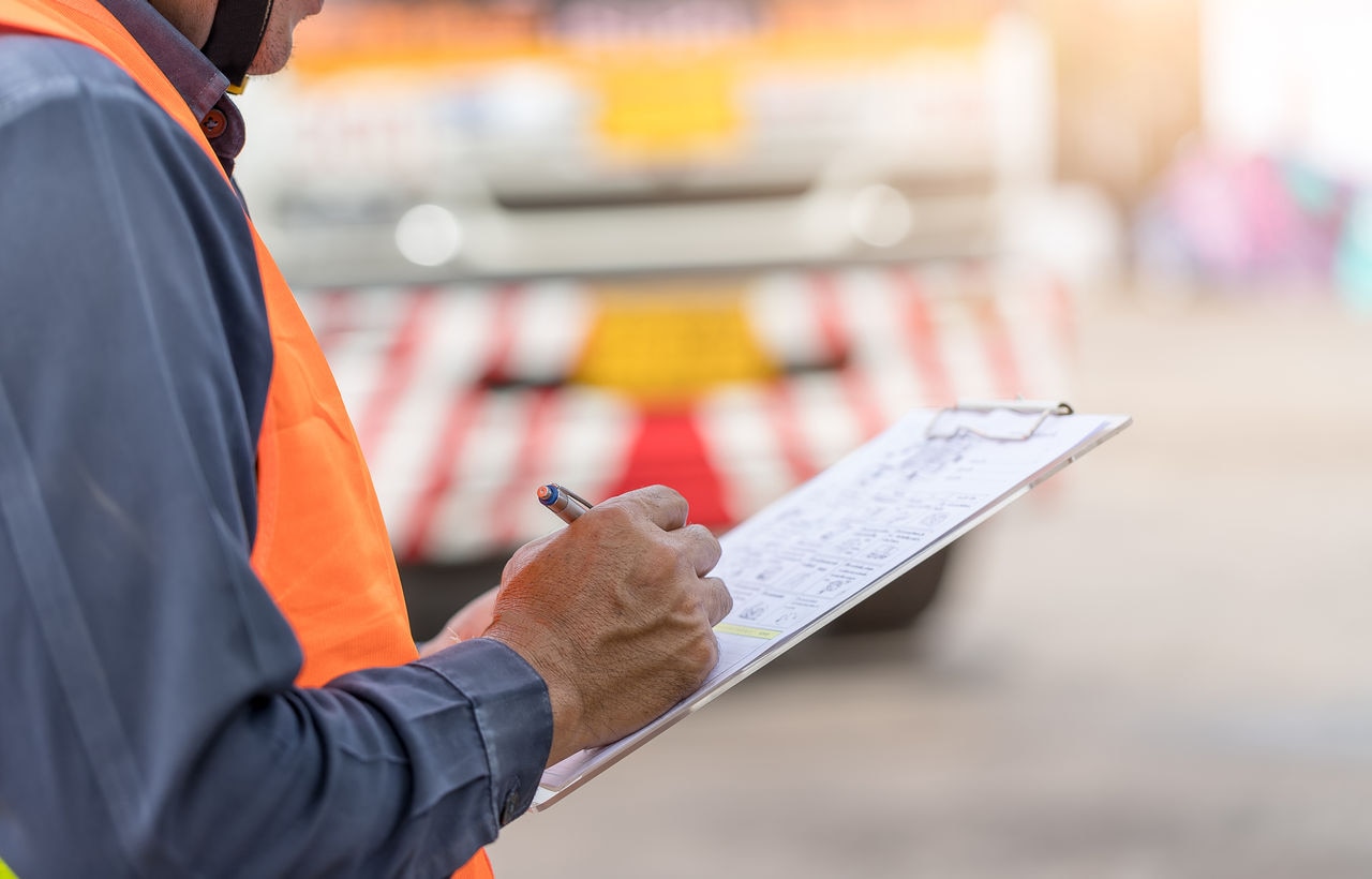 Performing a pre-trip inspection on a truck. Concept preventive maintenance truck checklist. Truck driver holding clipboard with checking of truck, spot focus.