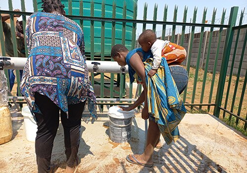 community members fill water buckets at community water station