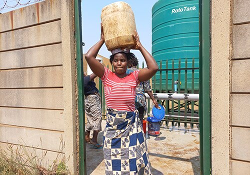 woman carries a water container from the community water station